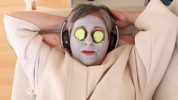 Woman with facial mask and cucumbers on face listening to music