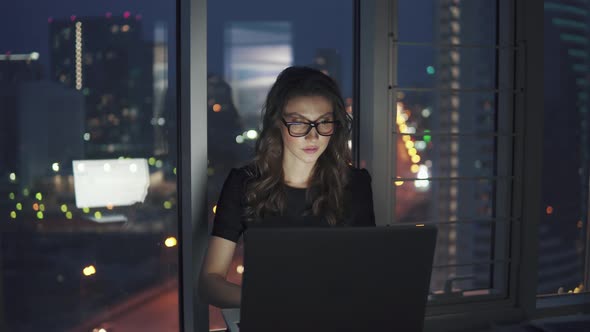 Young Business Woman Working Late in the Office. Portrait of a Girl with Glasses on the Background