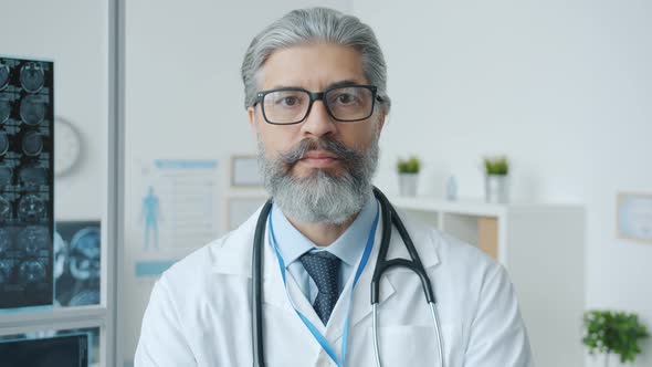 Portrait of Experienced Doctor Wearing Glasses and Uniform Standing in Clinic