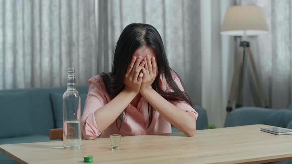 Drunk, Depressed Asian Woman With Smartphone On Table Pouring Vodka In A Shot Glass Before Drinking