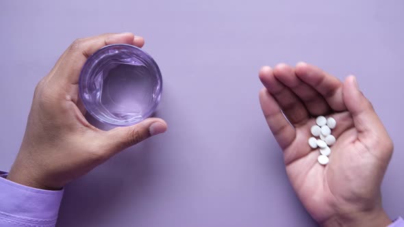 Young Man Holding Pills and Glass of Water on Purple Background