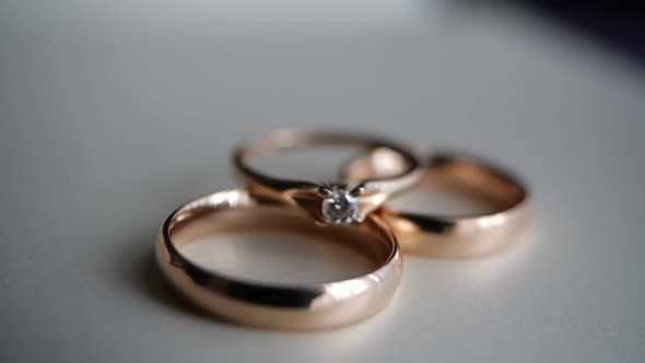 Three Beautiful Gold Rings - an Engagement with a Diamond and a Wedding Ring Lie on a White Table