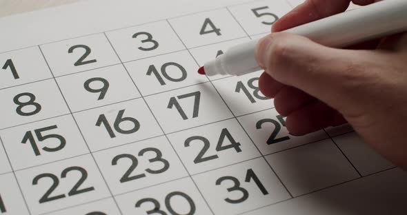 Man's hand Write down the 17th day on the paper calendar using a red pen.