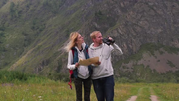 Couple in Love Travels in the Mountains with a Map and Binoculars. Friends Travelers Are Looking for