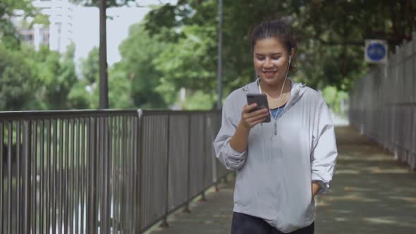 Portrait beautiful young Asian woman fitness runner walking and using mobile phone.