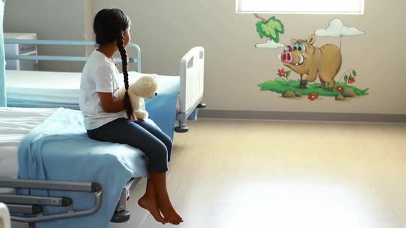 Sick girl sitting on bed with teddy bear