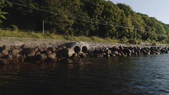 Orbiting Shot of Drainage Pipes Surrounded Rocks By the River