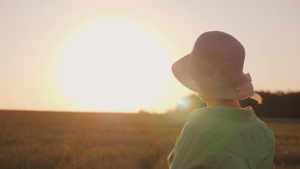 A Female Farmer in a Hat Looks at the Horizon Above a Field of Wheat