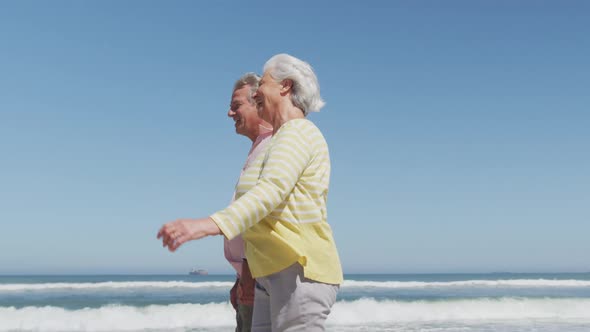 Happy senior caucasian couple holding hands talking to each other while walking on the beach