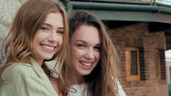 Two young beautiful smiling hipster girls in trendy clothes posing outdoors