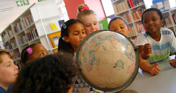Schoolkids looking at globe in the school library 4k