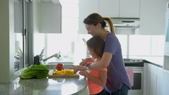 Mother teaching daughter to chop vegetables in kitchen