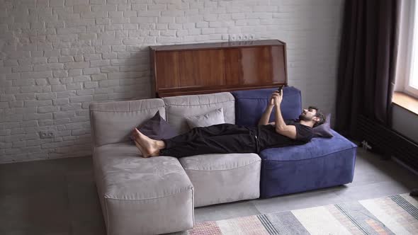 Man Lying on Couch Using Smartphone Scrolling Various Gestures Like Swiping and Scrolling