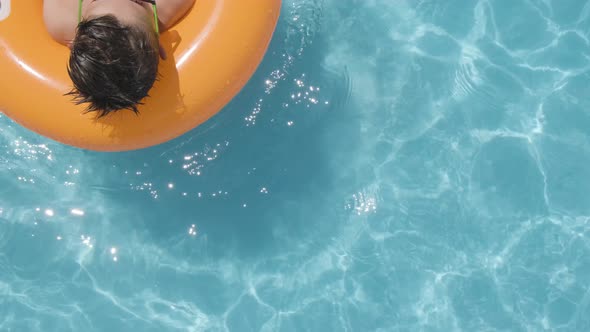 Caucasian Boy wearing sunglasses using Smartphone on Orange floater in the Swimming pool, Top down v