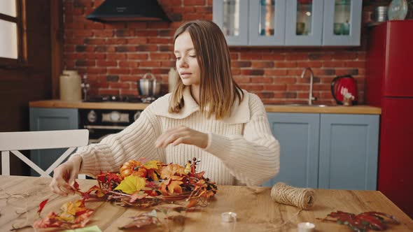 Young Woman Making Decorative Wreath of Orange Autumn Leaves Pumpkin Pine Cones