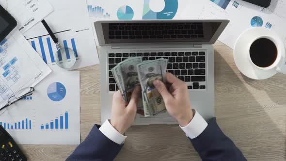 Male in Suit Sitting at Desk and Counting Dollar Bills in Hands, Successful Deal