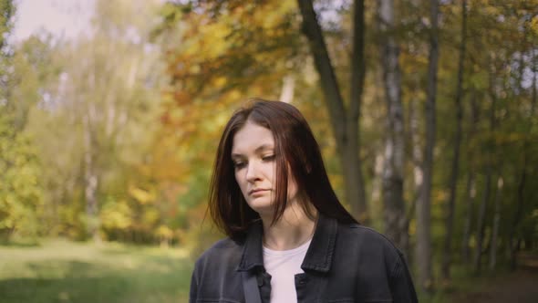 Woman in the Fall Walks Along Path in the Park Twists Her Hair on Her Finger