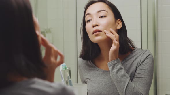 Handsome Asian woman looking at her skin at the mirror and combing hair