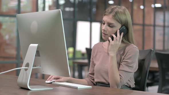 Young Woman Talking on Smartphone and Sitting on Office Desk 