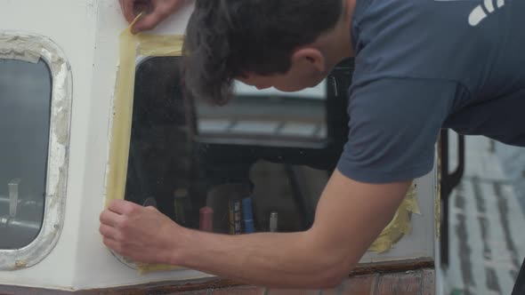 Young carpenter masking around aluminium wood boat windows to seal with waterproof sealant