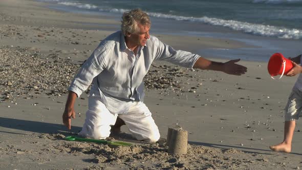 LS OF A WOMAN PHOTOGRAPHING A GRANDFATHER AND GRANDSON MAKING SANDCASTLES