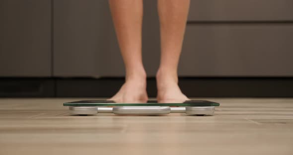 Male checking body weight on scales in kitchen. 