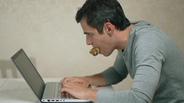 Man with a Cupcake in His Mouth Working on a Laptop