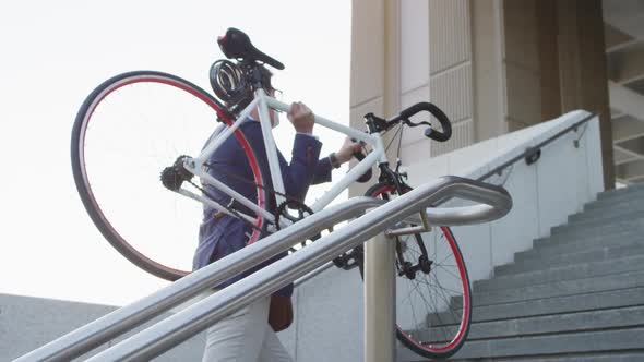 Asian man wearing face mask carrying bicycle while climbing up the stairs at corporate park