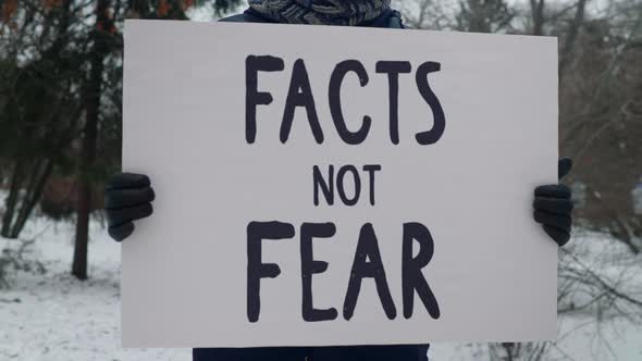 Man is standing in snow and holding sign with the phrase facts not fear. Protest