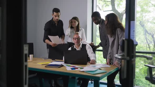 Professional Caucasian Man Sitting at Table with Laptop Talking As Multiethnic International Team