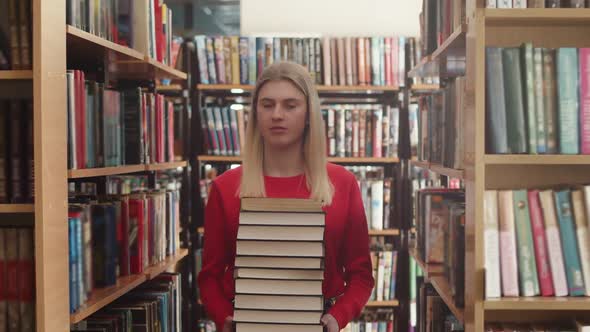 Female student rides in library among shelves with books with stack of textbooks at hands