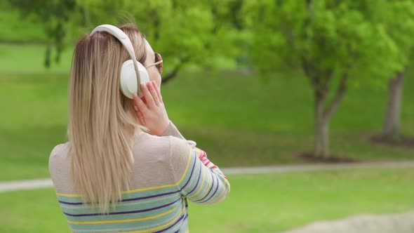 Woman in White Wireless Headphones Enjoying Morning in Green City Park at Summer
