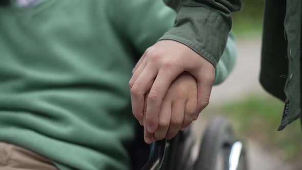 Closeup Child Hand on Wheelchair Armrest with Unrecognizable Girl Touching Palm of Disabled Friend