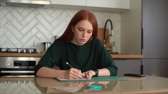 Front View of Focused Young Woman Student Making Mark with Pencil on White Paper Lying on Green