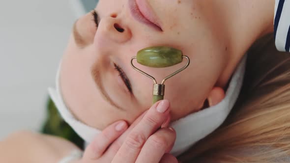 Close-up Shot of Facial Massage with a Jade Roller on Woman's Face at Beauty Salon