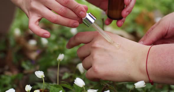 female hands drip serum from a pipette onto hands, greenery and flowers background, natural eco