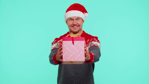 Cheerful Man in Santa Sweater Presenting One Christmas Gift Boxes Stretches Out His Hands to Camera