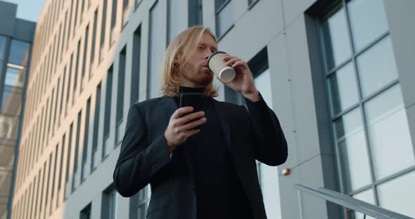 Bottom View of Successful Businessman Drinking Coffee From Paper Cup and Using Smartphone. Cheerful