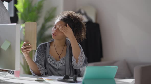 Young African American Woman Looking in Mirror in the Morning As Man Passing at Background Sitting