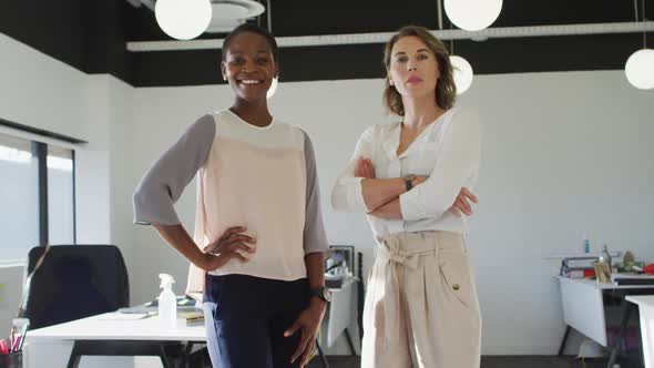 Two diverse female colleagues standing and smiling in office