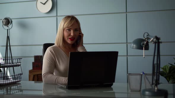 Businesswoman Is Talking By Mobile Phone and Working with Laptop in Office Room