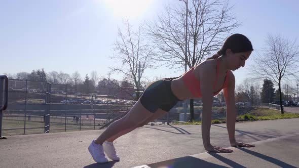 Athletic young woman doing pushups on curb with bright sun behind