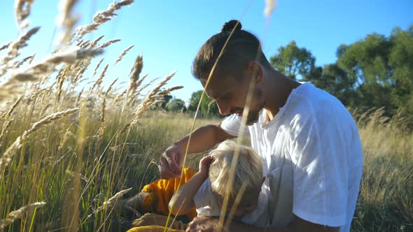 Young Father Holding in Hand Spikelet and Playing with Child at Meadow