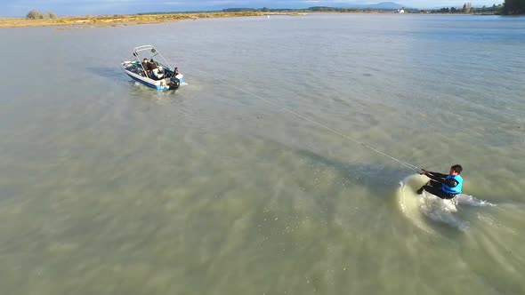 Aerial shot of a young man wake boarding in a lake with friends