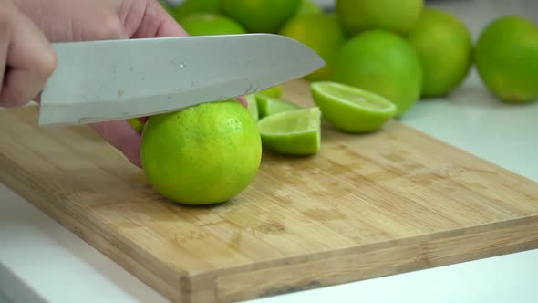 Hand Slicing fresh Lime With Knife On Wooden Board In Kitchen