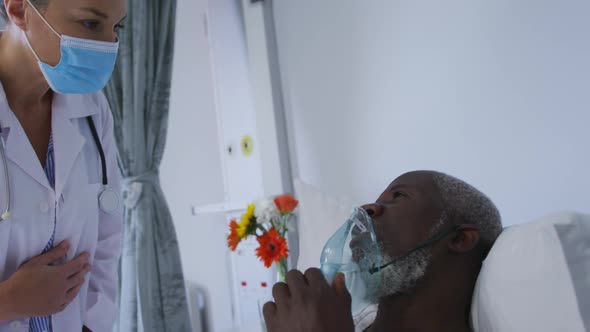 African american male patient in hospital bed wearing oxygen mask talking to doctor