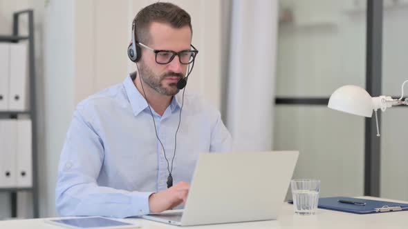 Middle Aged Man with Headset Talking While Working on Laptop