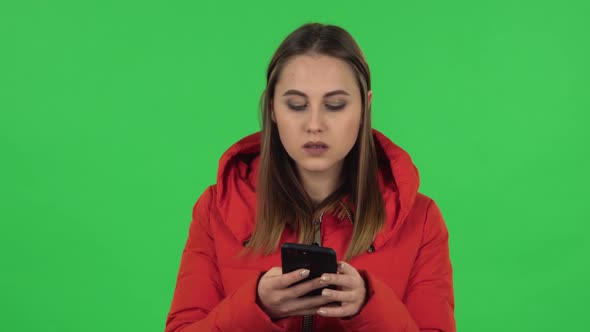 Portrait of Lovely Girl in a Red Down Jacket Is Texting on Her Phone. Green Screen