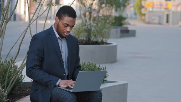 Focused African American Student Freelancer in Suit Sitting Outdoor Holding Laptop on Knees Study