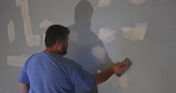 Worker Sanding the Drywall Mud Using Sand Trowel During Renovation the House